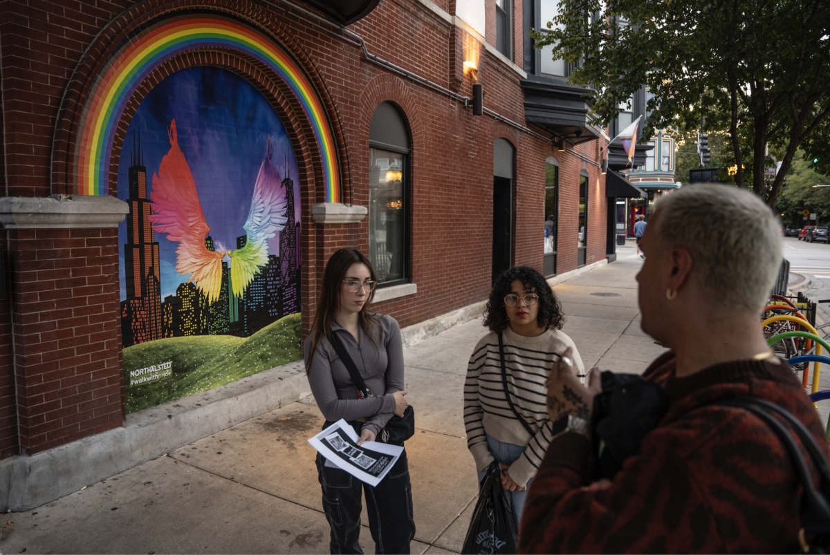 Coordinator of student support at the student diversity and inclusion office Matthew Rillie speaks to first year creative writing major Lyn Serrano and first year theatre tech and design major Lexie Cramer about the mural "Wings of Pride" on W. Roscoe St. in Northalsted on Tuesday, Oct. 1, 2024.